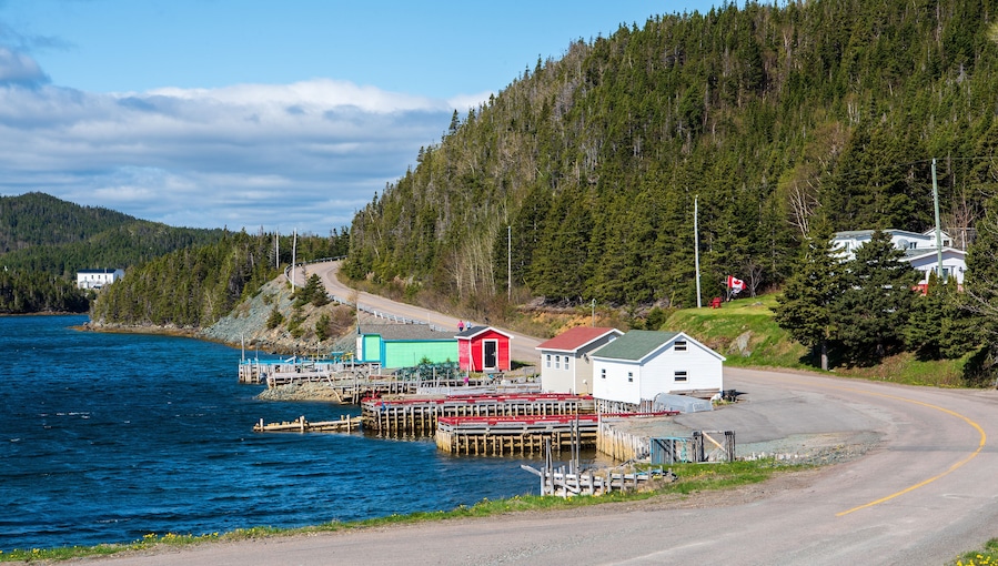 A coastal village with a pier, a red and white building, and a forested hill.