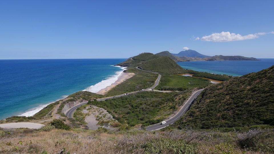 A coastal road winding through a mountainous landscape with a beach and ocean.