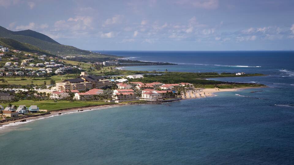 A coastal town with buildings near the beach and a mountain in the background.