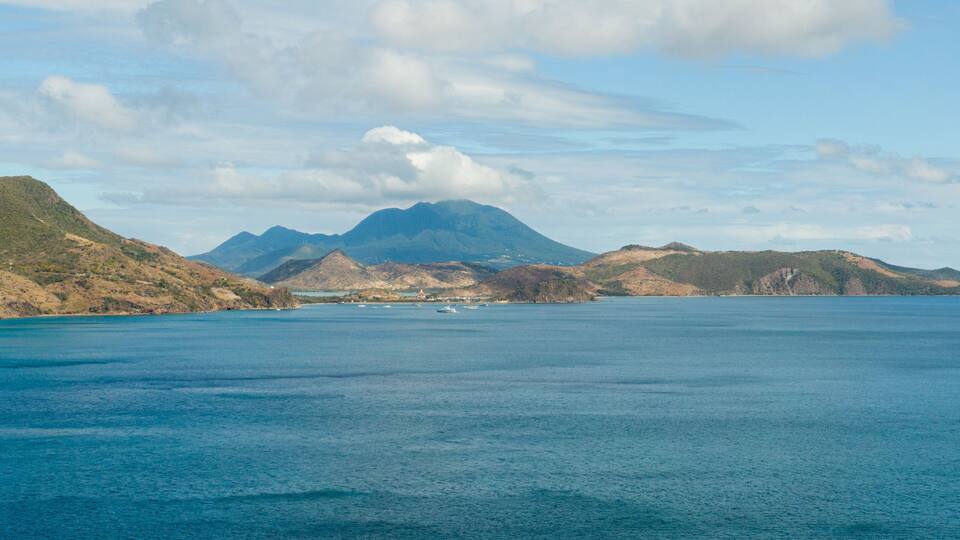 A coastal landscape with a large body of water, a prominent mountain, and several boats.