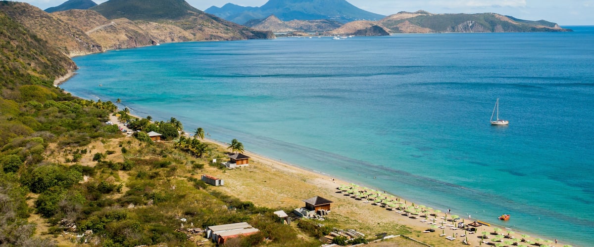 A coastal landscape with a beach, clear blue waters, and distant mountains.