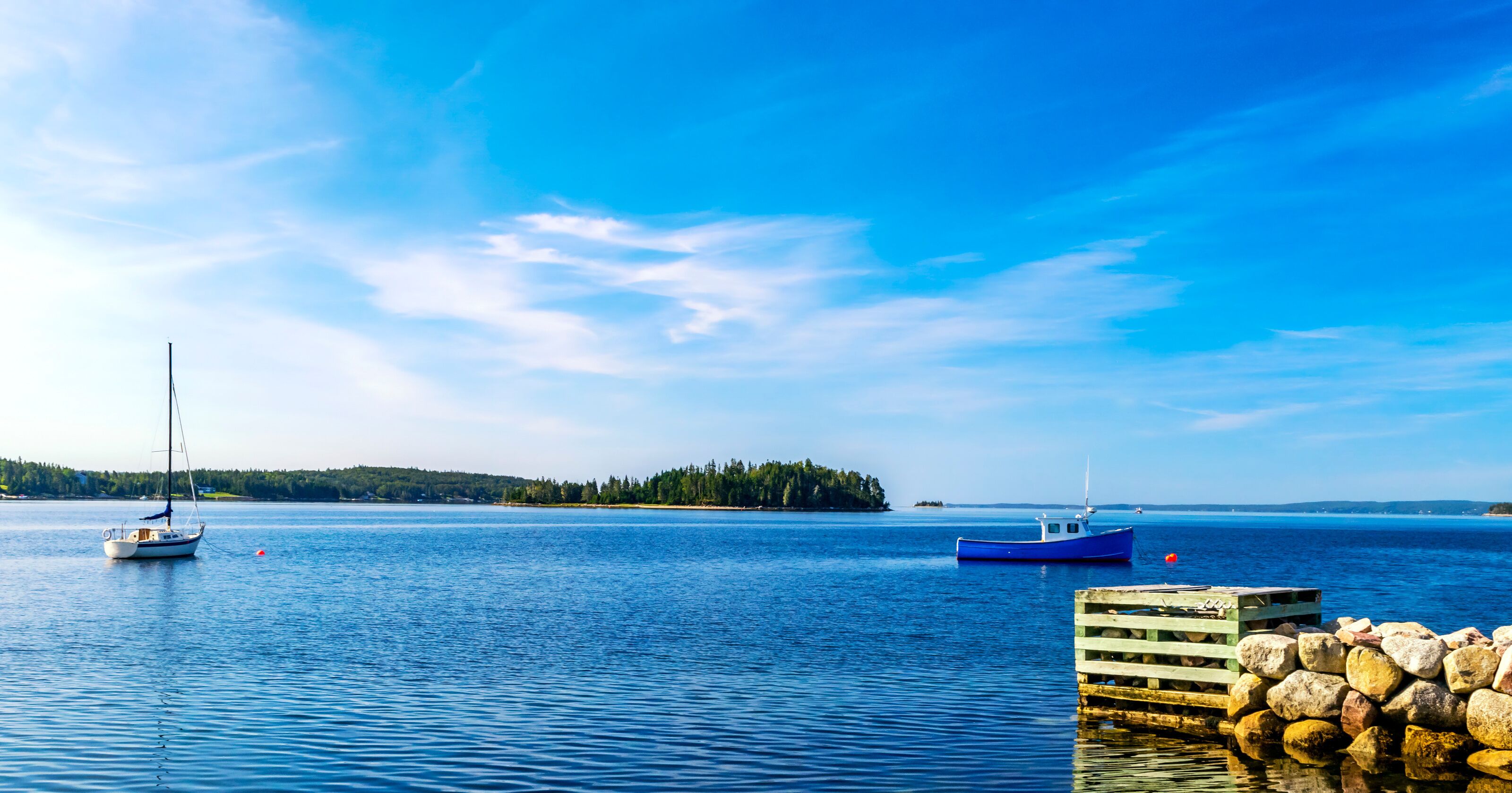 A calm lake with two boats, a dock, and a forested island in the distance.