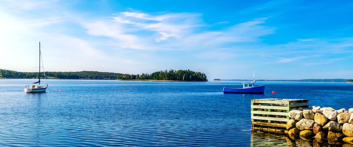 A calm lake with two boats, a dock, and a forested island in the distance.