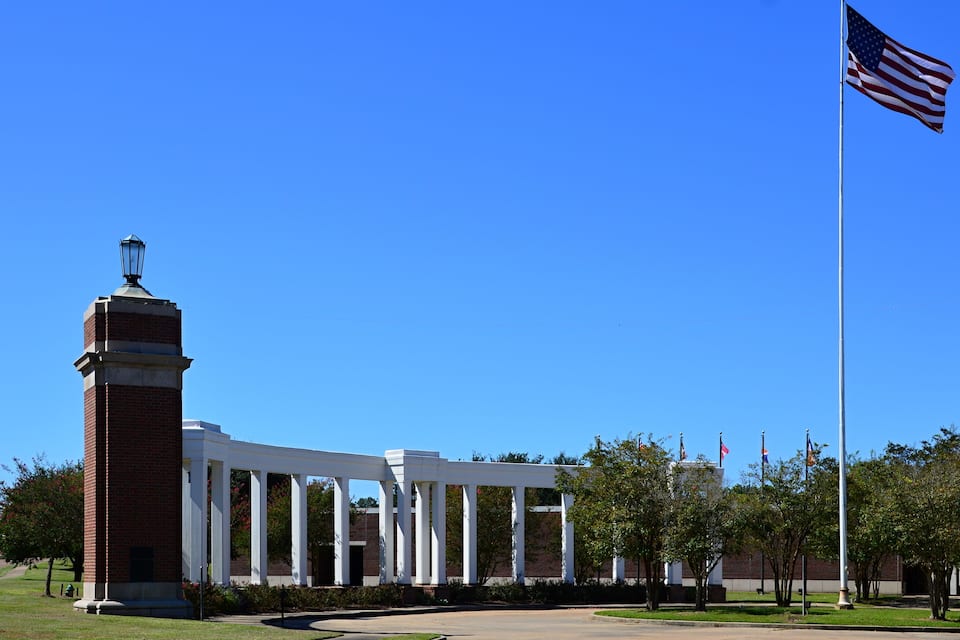 A building with white columns and a brick tower, an American flag, and a clear blue sky.