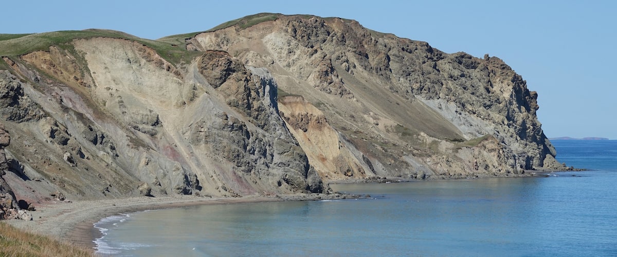 A coastal landscape with a rocky cliff and a sandy beach.