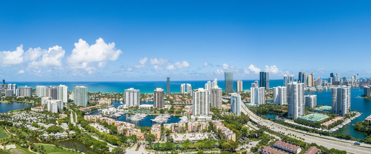 A coastal cityscape with high-rise buildings, marina, and golf courses.