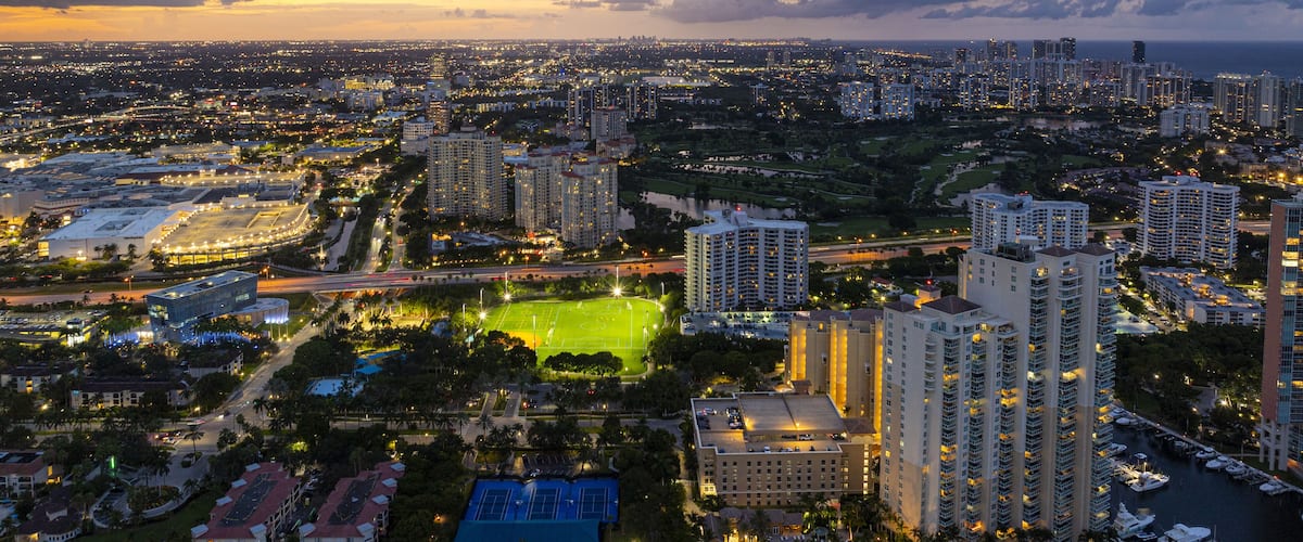 Aerial view of illuminated buildings casting golden glows against the deepening blues of twilight in the vibrant cityscape, Aventura, Florida, United States.