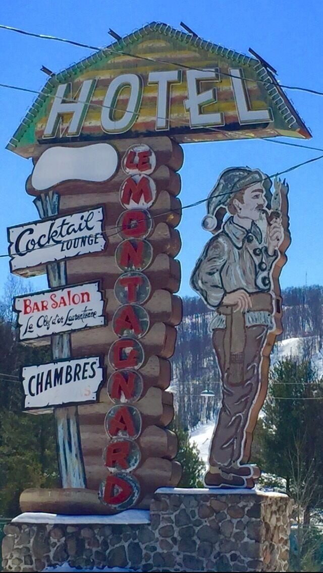 Ein hölzernes Schild mit 'HOTEL' oben, 'LE MONTAGNE' in der Mitte und 'Cochon Lounge', 'Bar Salon' sowie 'CHAMBRES' an den Seiten.