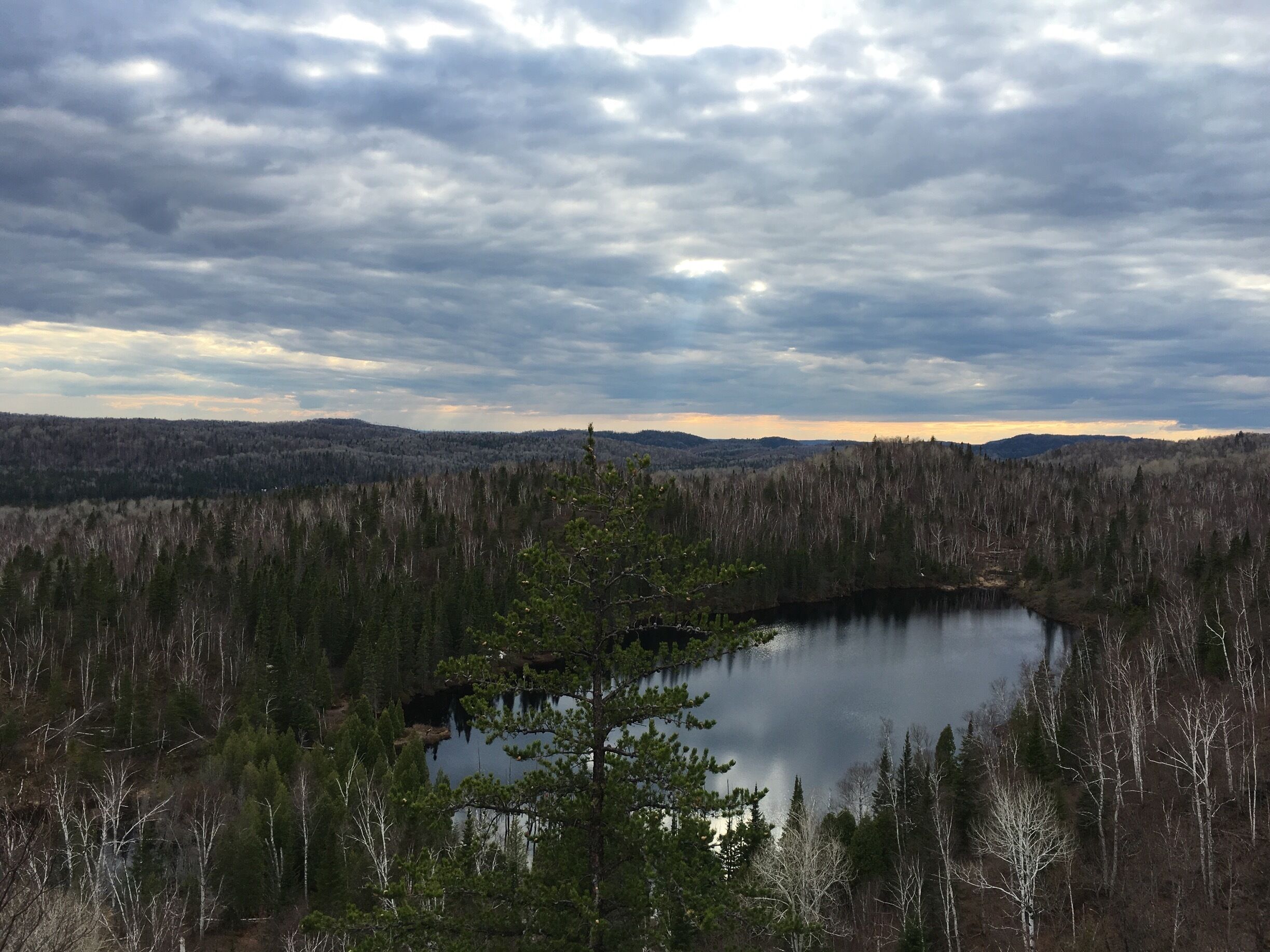A lake surrounded by dense forest and distant hills under a cloudy sky.