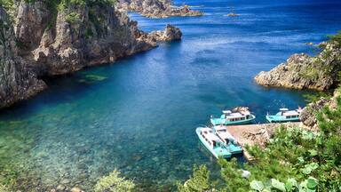 A coastal area with clear blue waters, rocky cliffs, and turquoise boats docked near the shore.