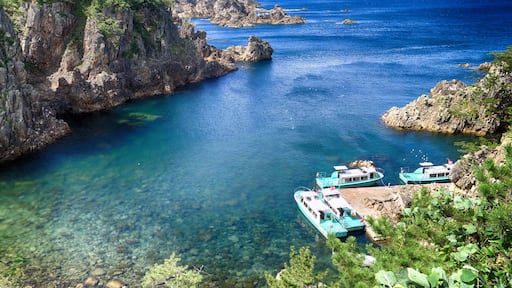 A coastal area with clear blue waters, rocky cliffs, and turquoise boats docked near the shore.