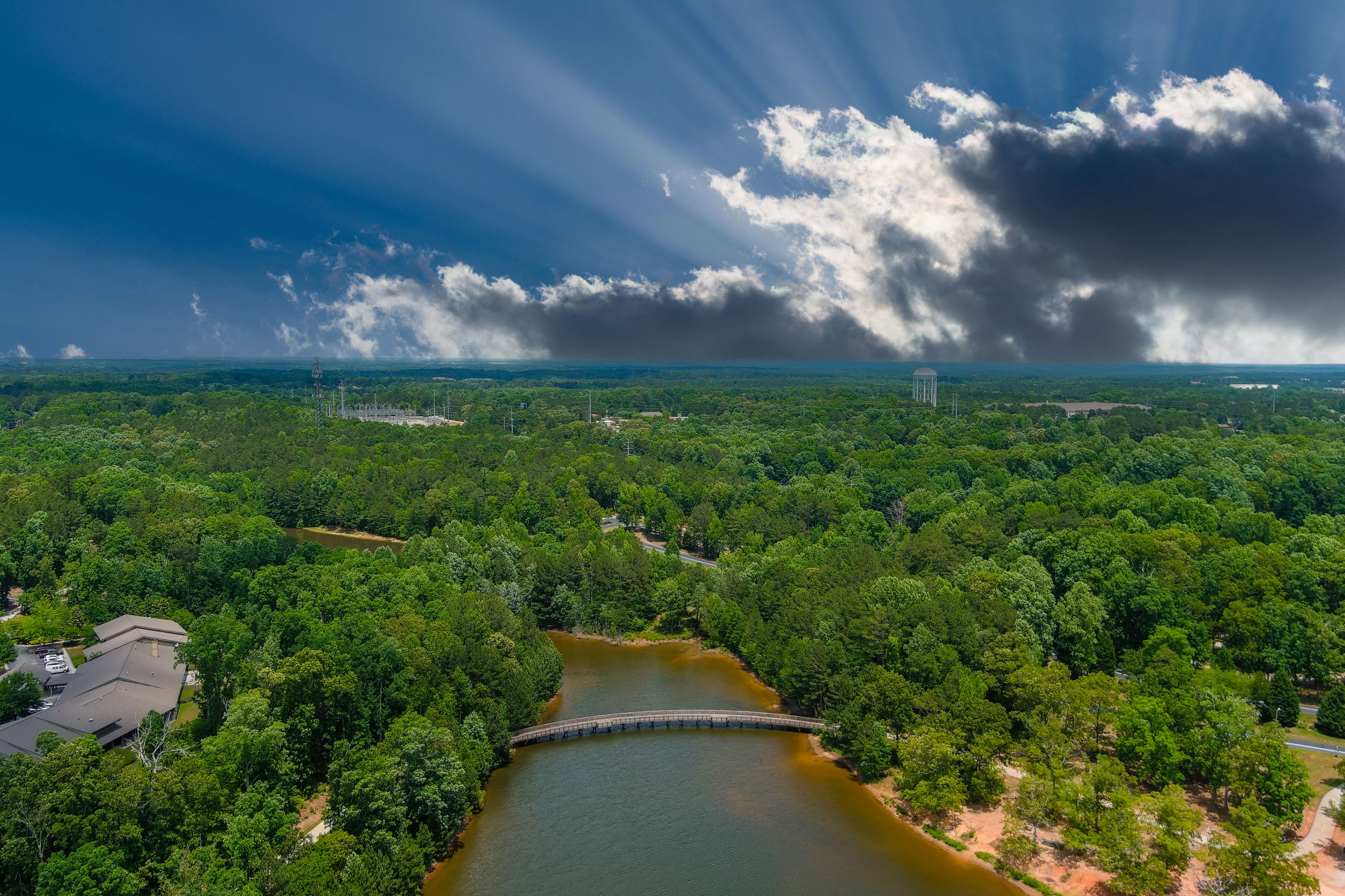 a gorgeous aerial shot of the rippling lake water surrounded by lush green trees, grass and plants with a gorgeous blue sky and powerful clouds at Indian Lake at Lake Spivey Recreation Center