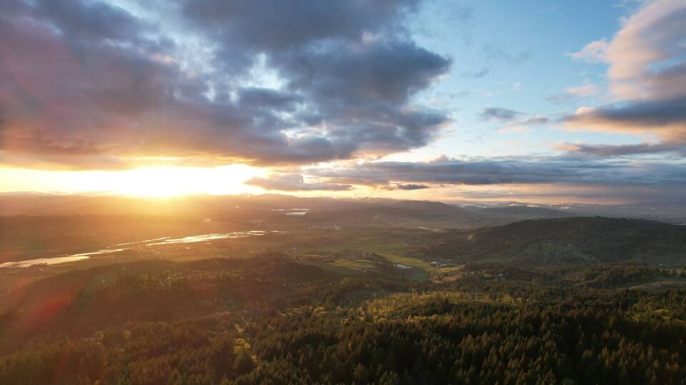 A sunset over a forested valley with a river and distant hills.