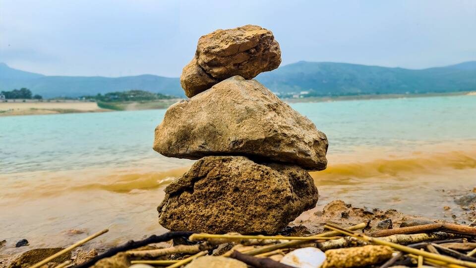 A stack of rocks by a river with mountains in the background.