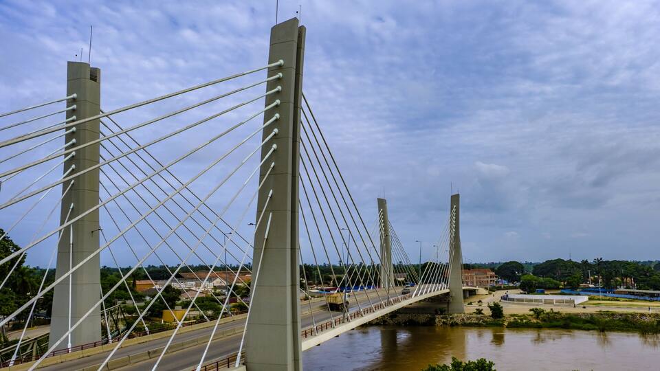 A cable-stayed bridge over a river with a cityscape in the background.