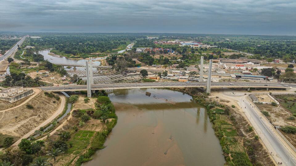 A bridge over a river with surrounding greenery and industrial buildings.