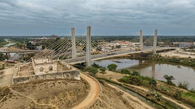 Uma ponte suspensa sobre um rio, com uma paisagem montanhosa e uma pequena cidade ao fundo.