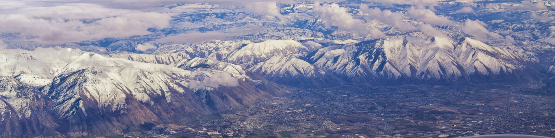 Aerial view from airplane of the Wasatch Front Rocky Mountain Range with snow capped peaks in winter including urban cities of Provo, Farmington Bountiful, Orem and Salt Lake City. Utah. United States