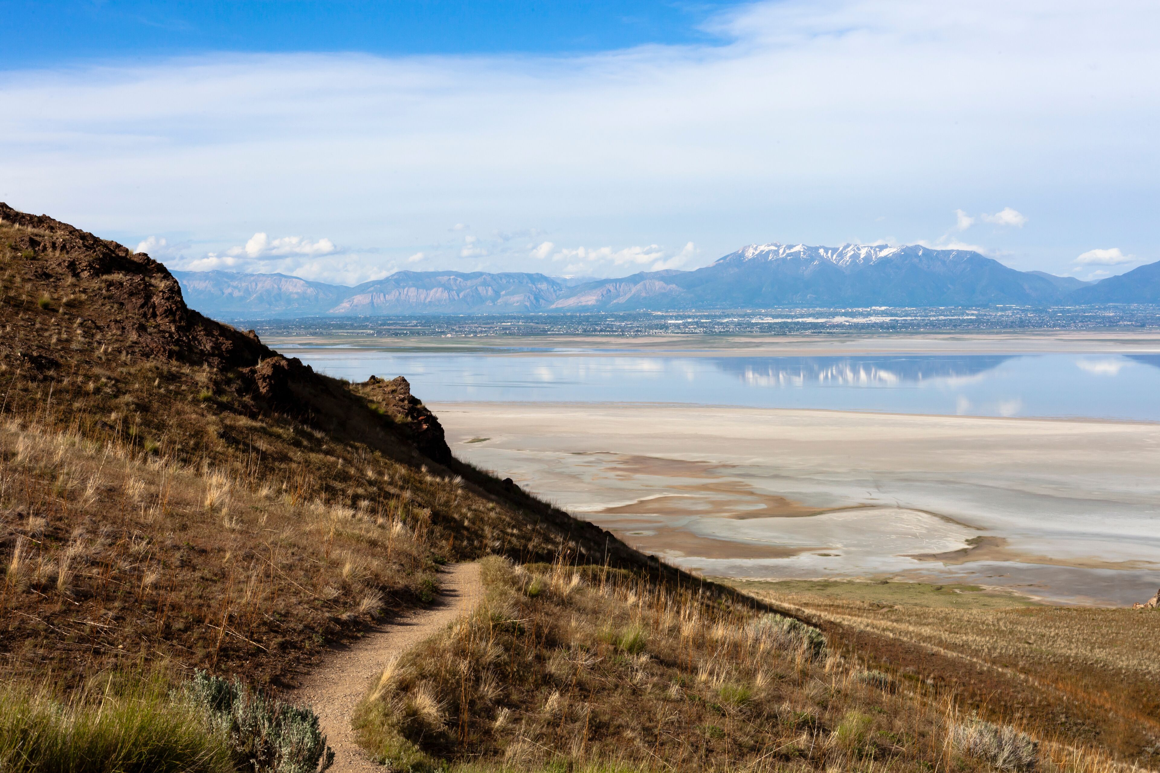 A mountainous landscape with a clear path leading to a calm lake reflecting the mountains.