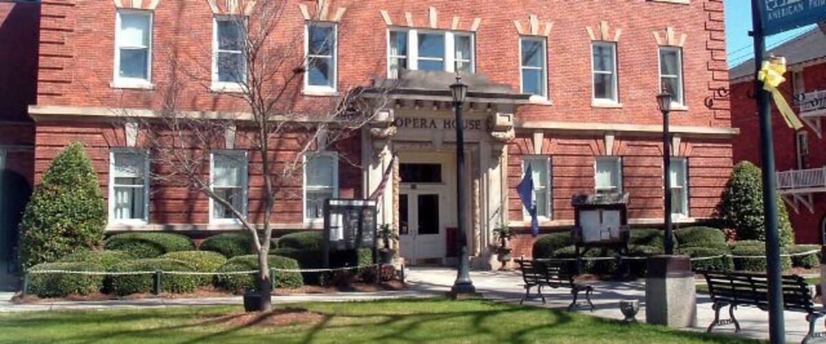 A red brick building with a sign reading "Opera House" and a flagpole with a flag.