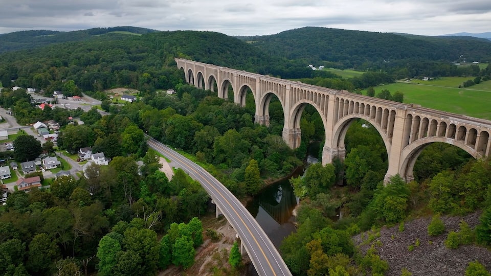 A large stone bridge over a river, surrounded by lush green hills and a small town.