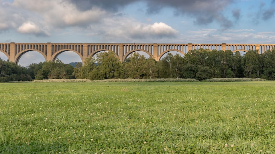 A large stone bridge with multiple arches spanning a river, surrounded by lush green fields and trees.