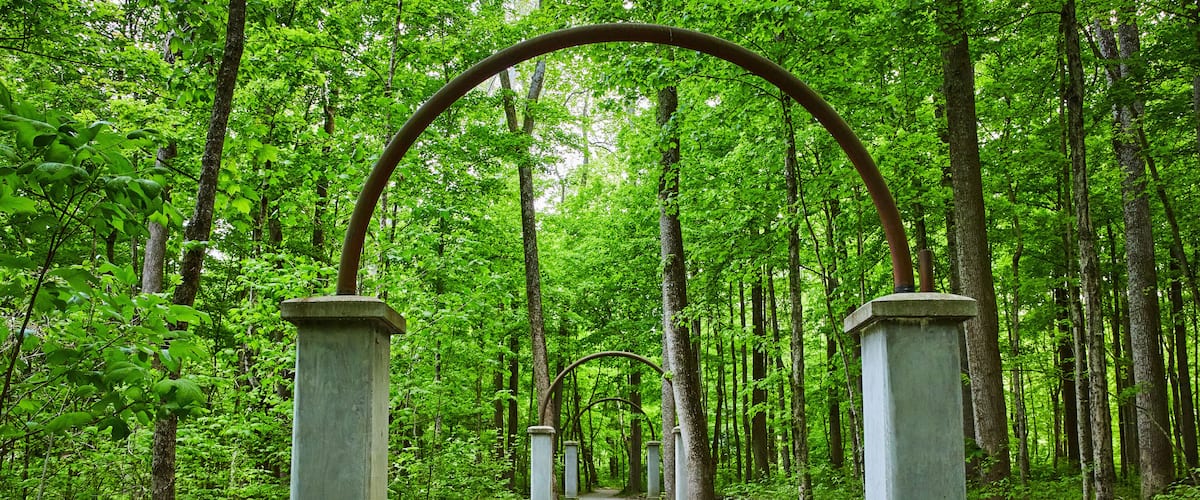 A forest path with a metal archway supported by concrete pillars.