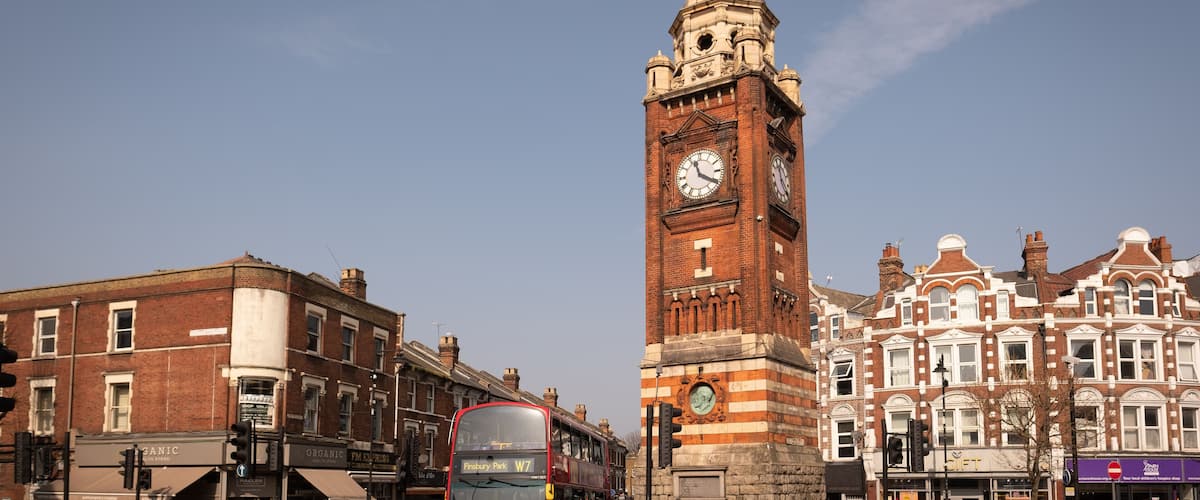 A red double-decker bus, a tall clock tower, and historic buildings.