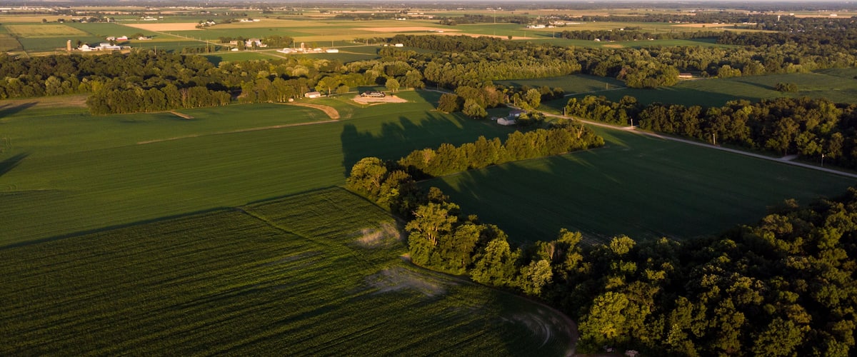 An aerial view of a rural landscape with fields, trees, and scattered buildings.