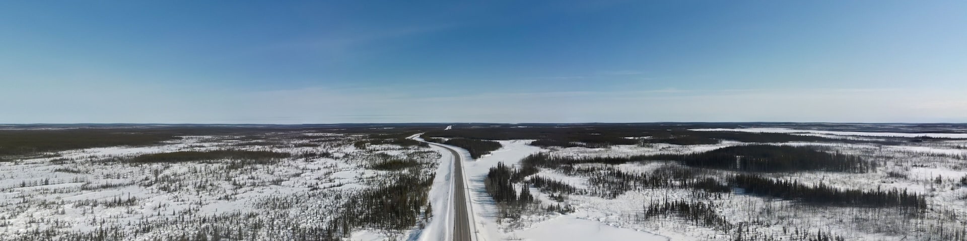 A snow-covered landscape with a winding road through a forest.