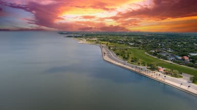 aerial shot along the coast of Lake Pontchartrain with homes, lush green trees, plants and grass, rippling water, powerful clouds at sunset in New Orleans Louisiana USA