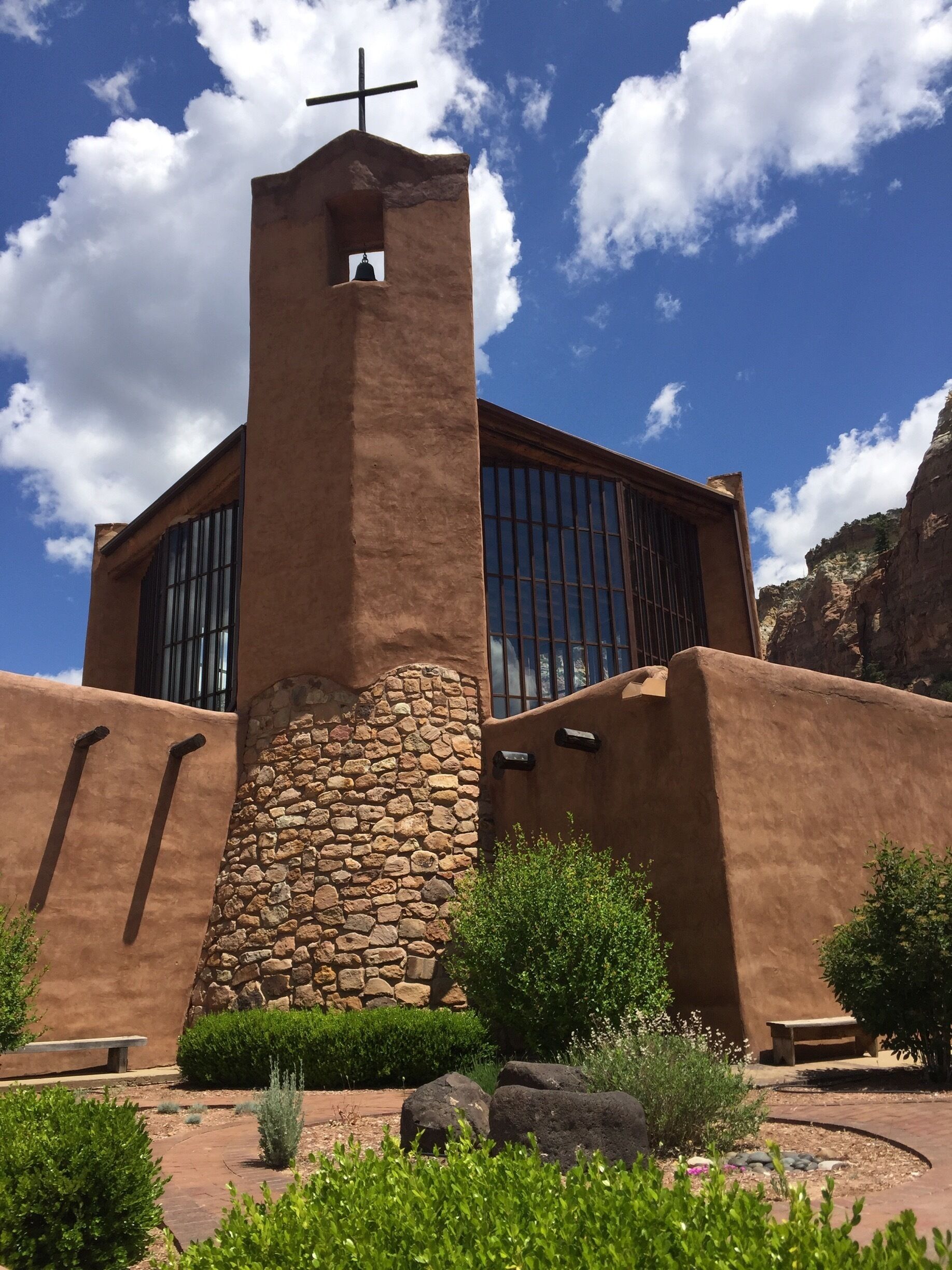 A church with a cross on top, a bell, and a stone base.