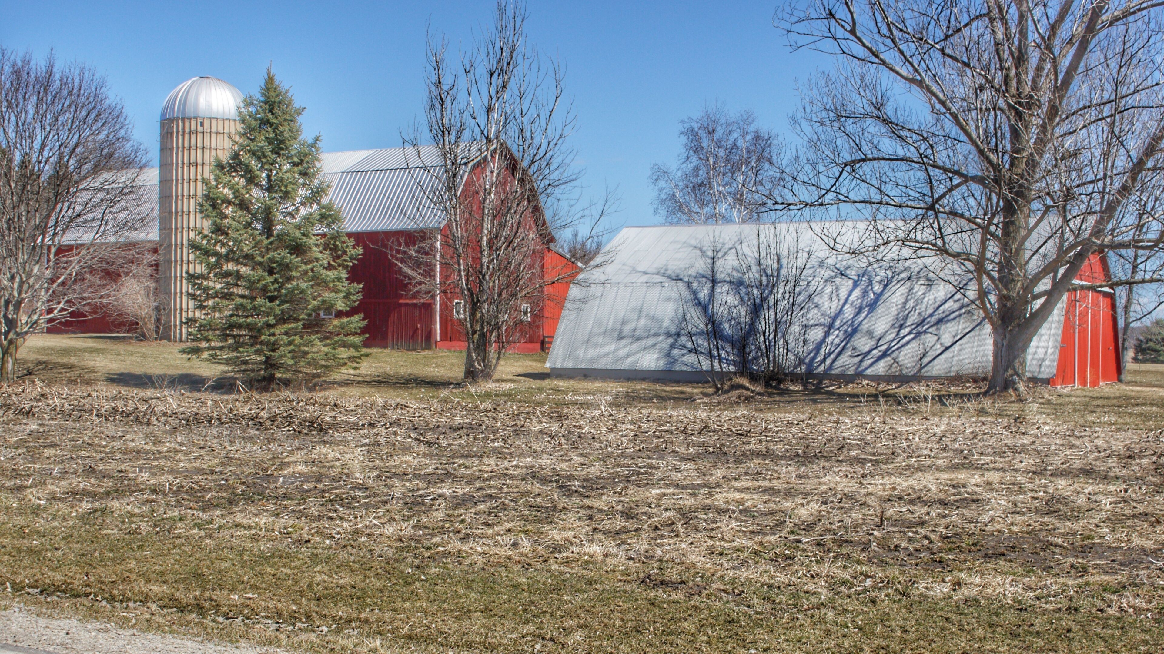 A rural landscape with a silo, barns, and a greenhouse.
