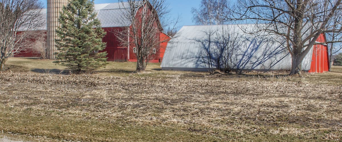 A rural landscape with a silo, barns, and a greenhouse.