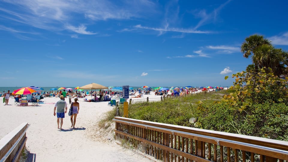 A crowded beach with people walking on the sand and colorful umbrellas.