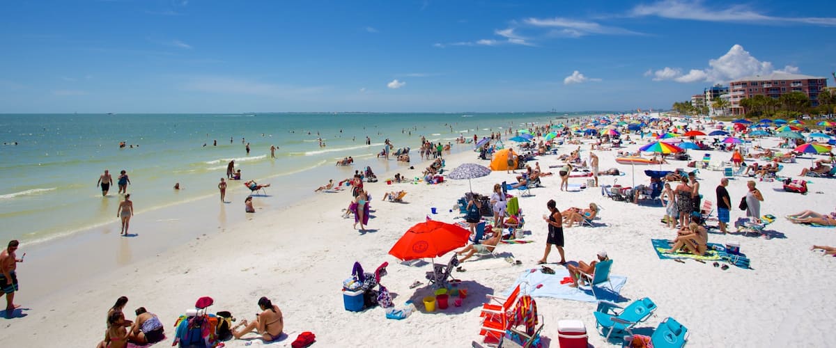 A crowded beach with people sunbathing and swimming.