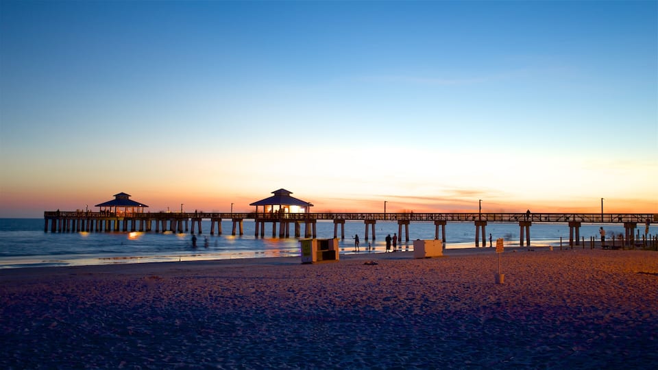 A pier extending into the ocean at sunset with two covered structures at the end.