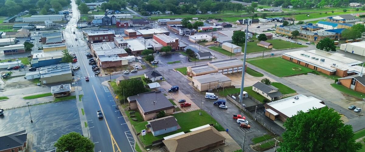 An aerial view of a small town with a main street, industrial buildings, and surrounding green fields.
