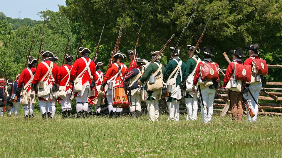 A group of reenactors in historical uniforms marching in a field.