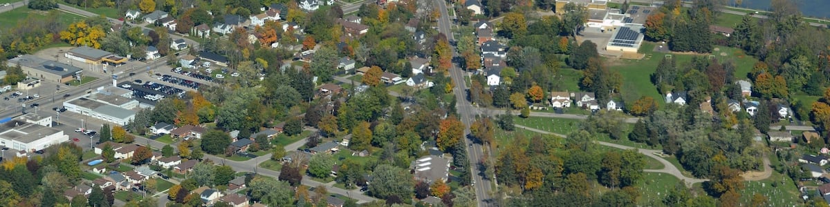 An aerial view of a town with a river, a bridge, and surrounding greenery.