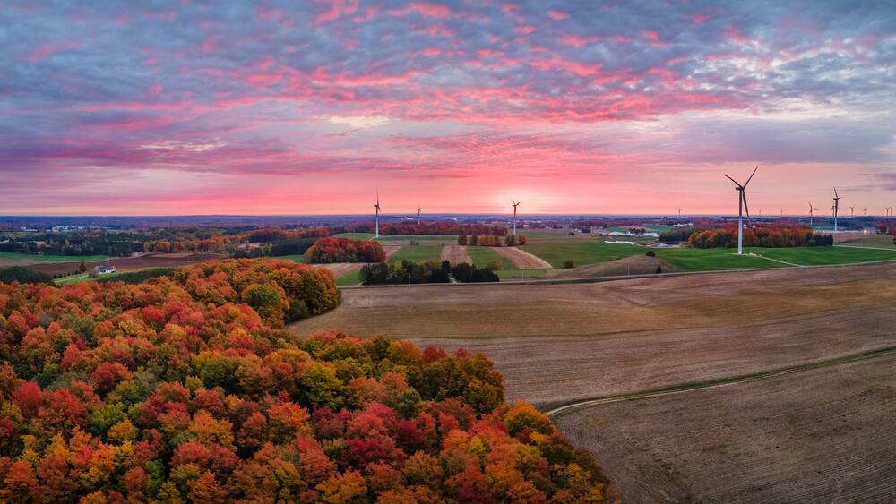 Un paysage aux couleurs automnales, avec des éoliennes et un coucher de soleil.