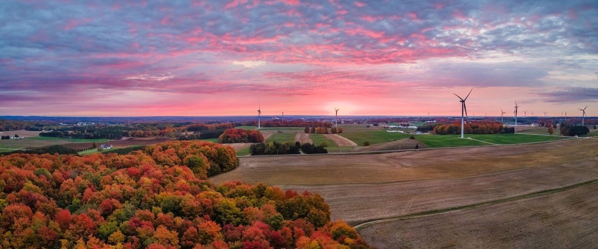 A landscape with autumn foliage, wind turbines, and a sunset.