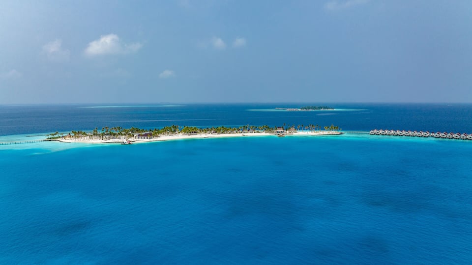 A tropical island with clear turquoise waters, a white sandy beach, and overwater bungalows.