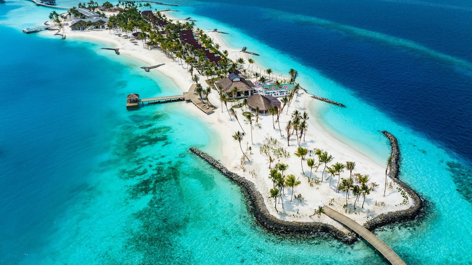 An aerial view of a tropical island with a white sandy beach, clear turquoise waters, and a wooden pier connecting to the mainland.