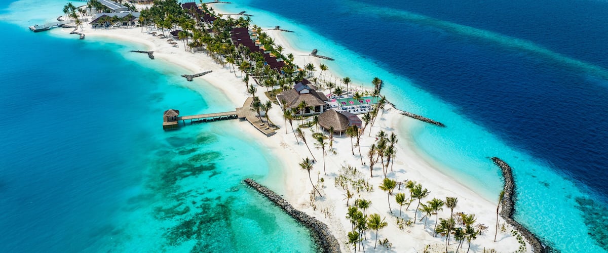 An aerial view of a tropical island with a white sandy beach, clear turquoise waters, and a wooden pier connecting to the mainland.