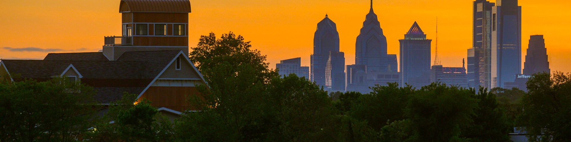 Un horizonte al atardecer con imponentes rascacielos y un edificio residencial con un techo característico.