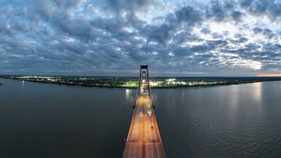 A river with a bridge, boats, and city lights in the distance.