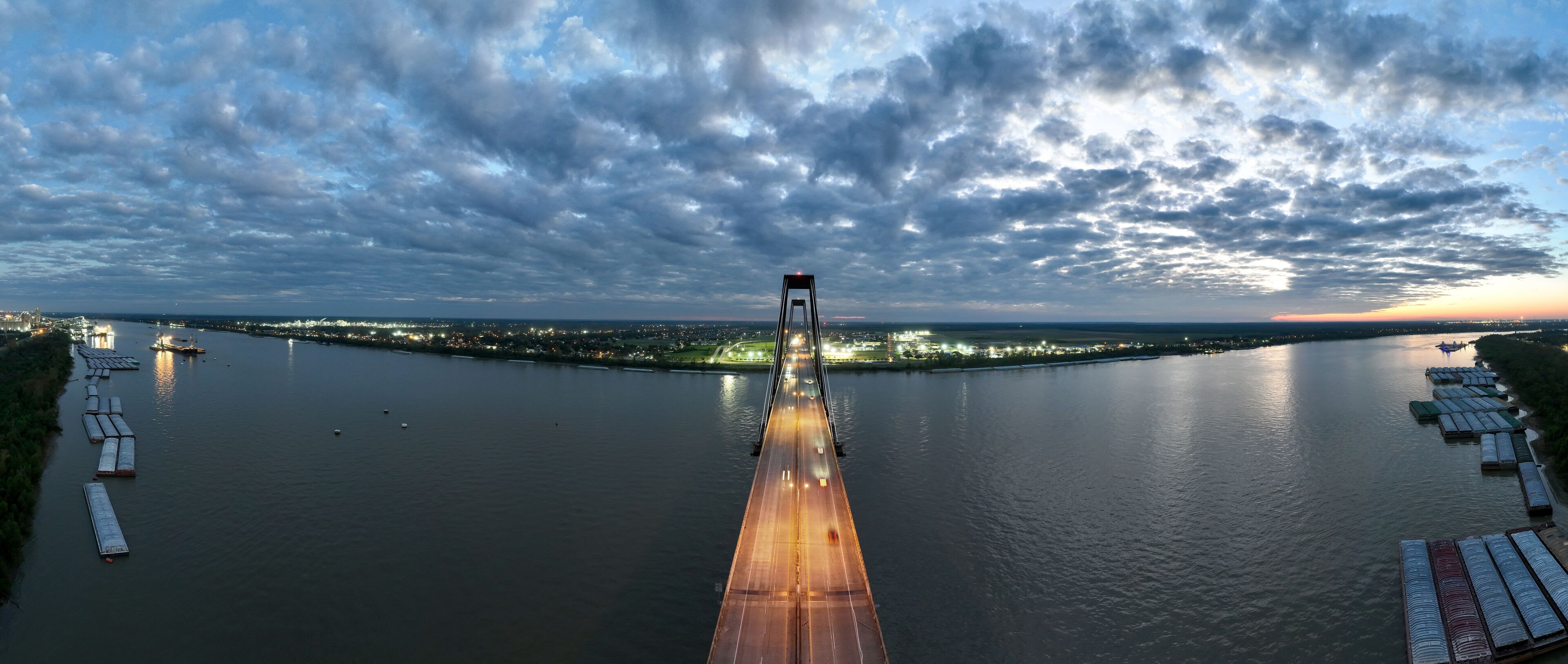 A river with a bridge, boats, and city lights in the distance.