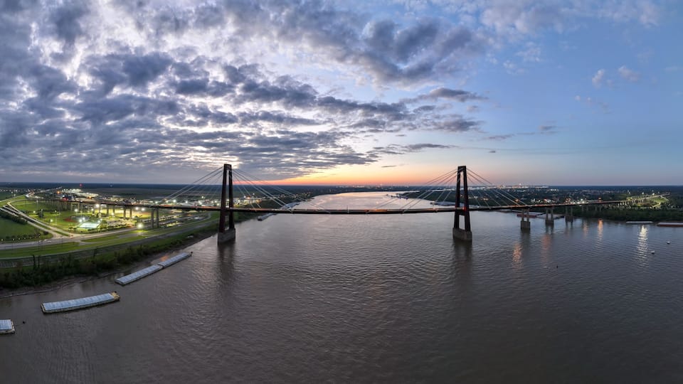 A large suspension bridge over a river with a sunset in the background.