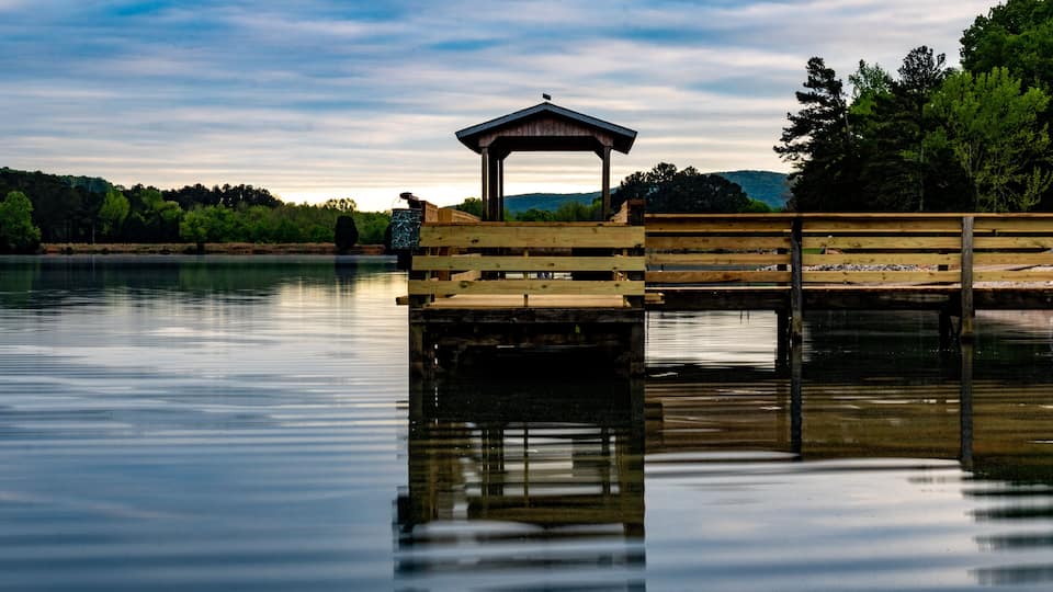 A wooden pier extending into a calm lake with a gazebo on one end and a bench on the other.